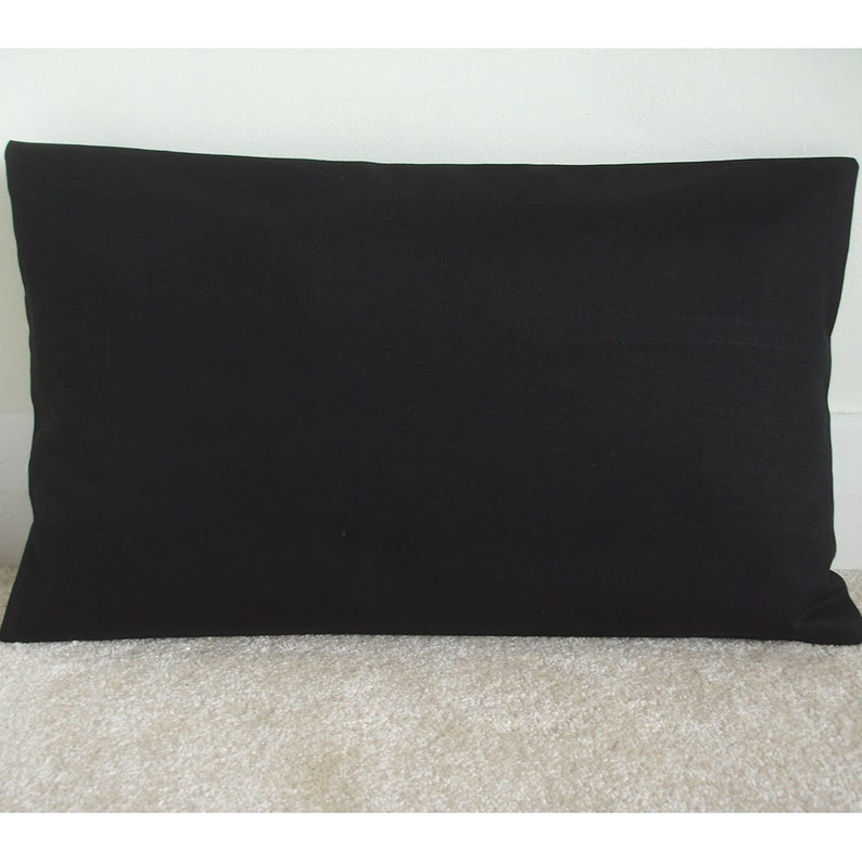 May include: A plain black pillow with a rectangular shape. The pillow is made of a soft, smooth fabric.