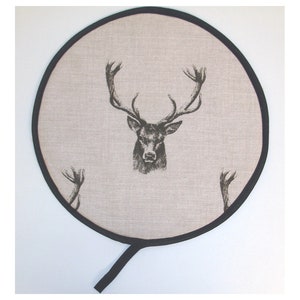 May include: Round beige pot holder with a black trim and a black and white stag print.