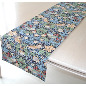 May include: A blue and green table runner with a floral and bird pattern. The runner features a repeating design of stylised birds, flowers, and leaves.