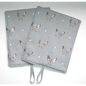 May include: Two grey fabric pot holders with a white and black chicken pattern and white dots. The pot holders have a loop handle.