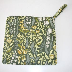 May include: A square fabric pot holder featuring a dark green background with a dense botanical print of white lily of the valley flowers, yellow blossoms, and various green foliage. The item includes a matching fabric loop for hanging.