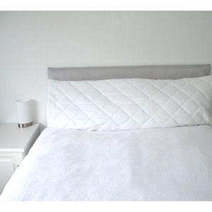 May include: A white quilted bedspread with a grey headboard and a white bedside table with a lamp.