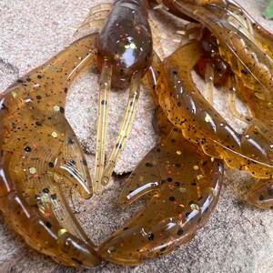 May include: A close-up of a pack of brown and gold fishing lures shaped like crawfish. The lures have black and red flecks throughout.