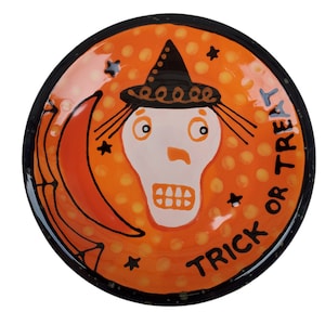May include: Orange ceramic plate with a black rim and a white skull wearing a black witch hat. The plate has yellow polka dots and the words "Trick or Treat" written in black.