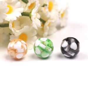 May include: Three round glass beads with white and gold accents. The beads are in shades of green, brown, and black.