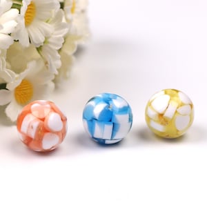 May include: Three spherical glass beads in orange, blue, and yellow. Each bead features a mosaic pattern of white and coloured segments. These beads are suitable for jewellery making or craft projects.