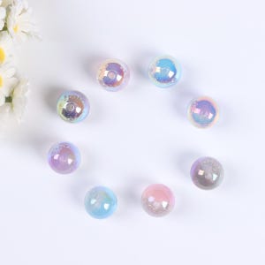 May include: Eight iridescent glass beads in various shades of blue, pink, and purple. The beads are round and have a smooth, glossy finish.