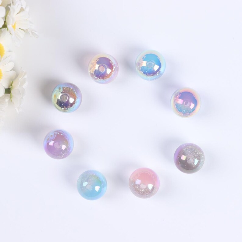 May include: Eight iridescent glass beads in various shades of blue, pink, and purple. The beads are round and have a smooth, glossy finish.