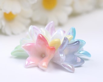 May include: A collection of iridescent pastel flower-shaped beads. The beads are made of glass and have a pearlescent finish. The beads are arranged in a circle, with the pink bead in the center.