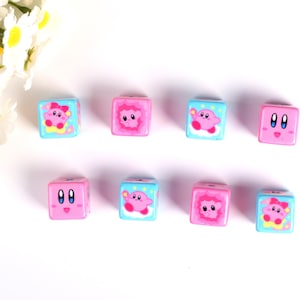 May include: Eight pink and blue dice with different images of a pink character on each side. The character is wearing a pink hat and has large eyes.