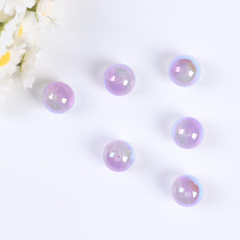 May include: Six iridescent purple glass beads with a hole in the center. The beads are scattered on a white surface.