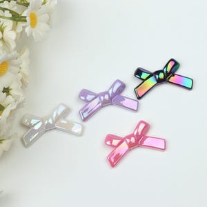 May include: Four iridescent plastic bows in different colors: white, purple, pink, and black. The bows are arranged on a white surface.