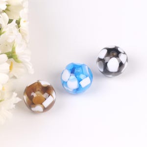 May include: Three round glass beads with white and colored patterns. The beads are blue, brown, and black.
