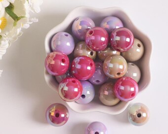 May include: A bowl filled with iridescent round beads in shades of pink, purple, and beige. The beads have a glossy finish and a small hole in the center.