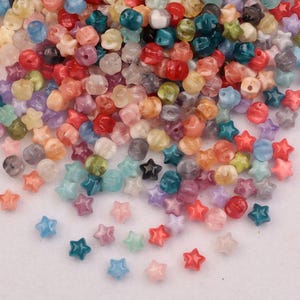 May include: A collection of colorful beads in various shapes, including stars and rounded forms. The beads are in shades of red, orange, pink, blue, green, and purple. These small beads are ideal for jewelry making and craft projects.