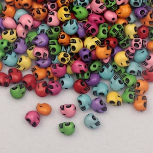 May include: A collection of colorful skull-shaped beads in various shades, including red, orange, yellow, green, blue, pink, and purple. Each bead has a detailed skull design. The beads are scattered, creating a vibrant and playful arrangement.