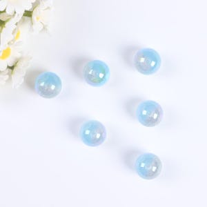 May include: Six iridescent blue glass beads with a hole in the center. The beads are scattered on a white surface.