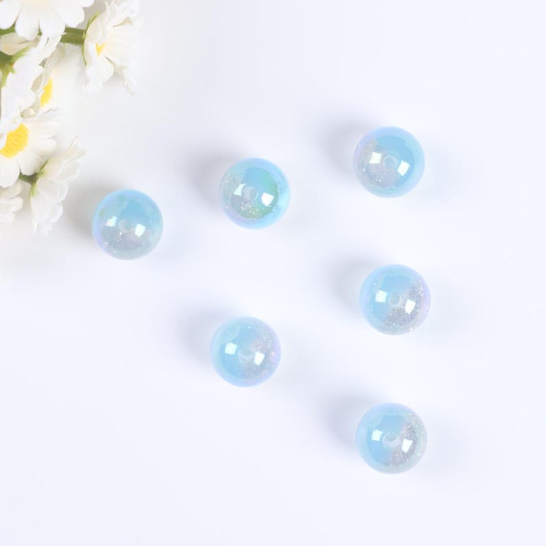 May include: Six iridescent blue glass beads with a hole in the center. The beads are scattered on a white surface.