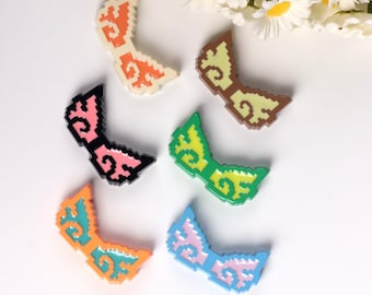 May include: Six pairs of pixelated sunglasses in various colors, including pink, green, blue, orange, brown, and cream. The sunglasses are made of plastic and have a pixelated design.