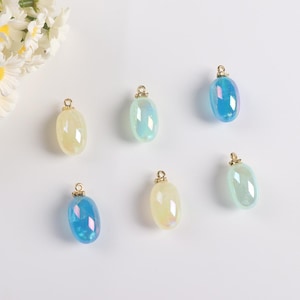 May include: Six iridescent glass oval charms with gold-tone metal loops. The charms are in shades of blue, green, and white.
