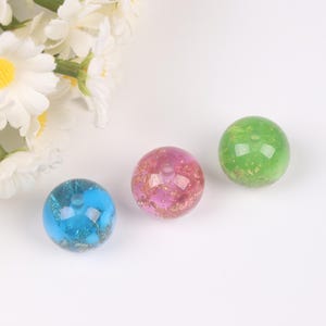 Puede incluir: Tres cuentas redondas translúcidas de resina en azul, rosa y verde. La cuenta azul tiene un efecto brillante, la cuenta rosa tiene copos dorados y la cuenta verde tiene copos dorados. Cada cuenta tiene un pequeño agujero.