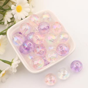 May include: A bowl filled with iridescent pastel pink and purple beads. The beads are round and have a smooth, glossy finish.