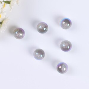 May include: Six iridescent glass beads with a glittery finish. The beads are round and have a hole in the center. They are a light purple color with a hint of blue.