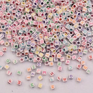 May include: A collection of small, square beads, each with a white base and multi-coloured letters. The letters are in various colours, including red, blue, green, and yellow. These alphabet beads are suitable for jewellery making and craft projects.