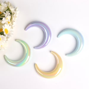 May include: Four iridescent crescent moon shaped ceramic ornaments in shades of light blue, lavender, and yellow.
