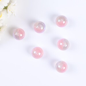 May include: Six iridescent pink glass beads with a hole in the center. The beads are scattered on a white surface.