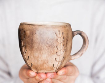 May include: A brown ceramic mug with a handle and a design of small branches on the side.