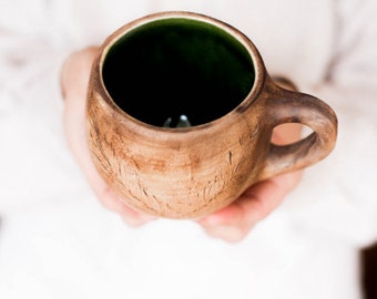May include: A brown ceramic mug with a green glazed interior. The mug has a handle and is decorated with a carved design.