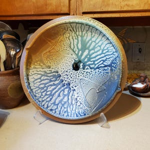 May include: A large, round ceramic serving dish with a blue, white, and brown glaze. The glaze has a swirling, abstract pattern.
