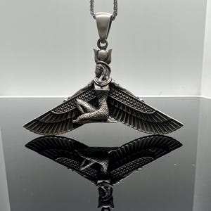 Peut inclure: Collier avec pendentif en argent représentant une représentation détaillée de la déesse égyptienne Isis avec des ailes déployées. Le pendentif est attaché à une chaîne en argent.