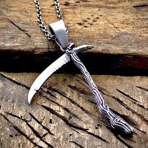 Może przedstawiać: Srebrny naszyjnik z zawieszką w kształcie sierpa. Zawieszka ma szczegółowy wzór i jest przymocowana do srebrnego łańcuszka.