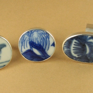 May include: Three silver rings with blue and white porcelain insets. The insets feature a bird, a tree, and a floral design.