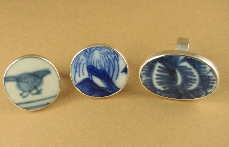 May include: Three silver rings with blue and white porcelain insets. The insets feature a bird, a tree, and a floral design.