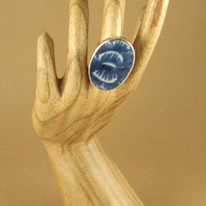 May include: A blue and white ceramic ring with a swirling pattern. The ring is on a wooden hand model.