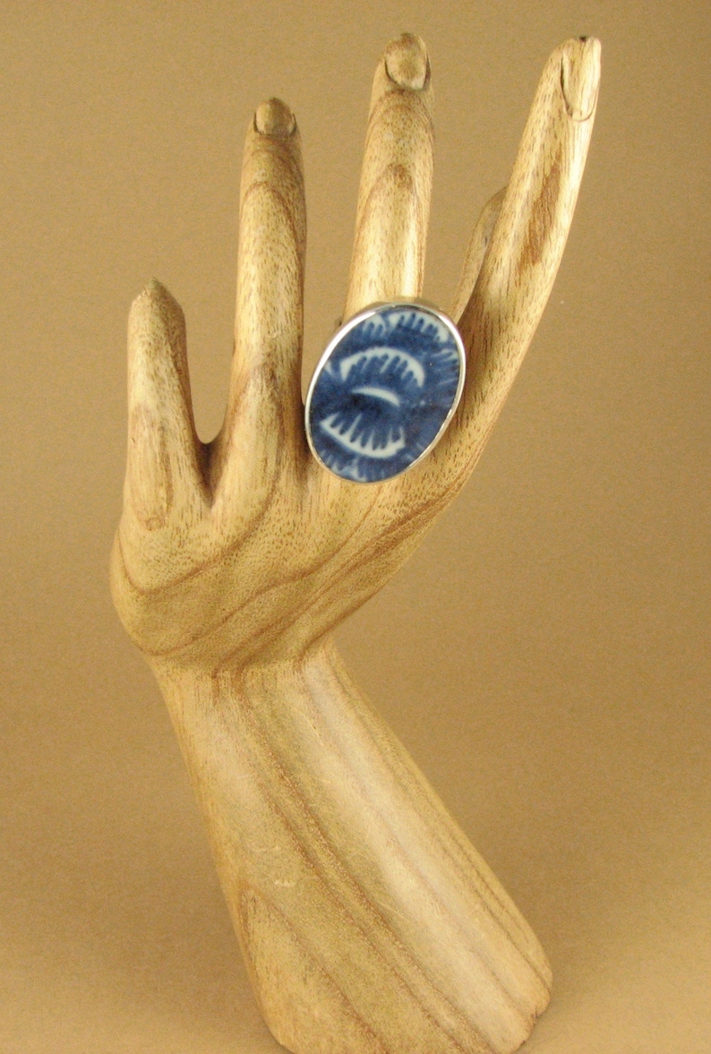 May include: A blue and white ceramic ring with a swirling pattern. The ring is on a wooden hand model.