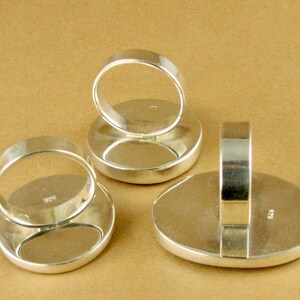 May include: Three silver rings with oval-shaped settings. The rings are shown from the back, revealing the silver bands and the markings "925" on the back of each ring.