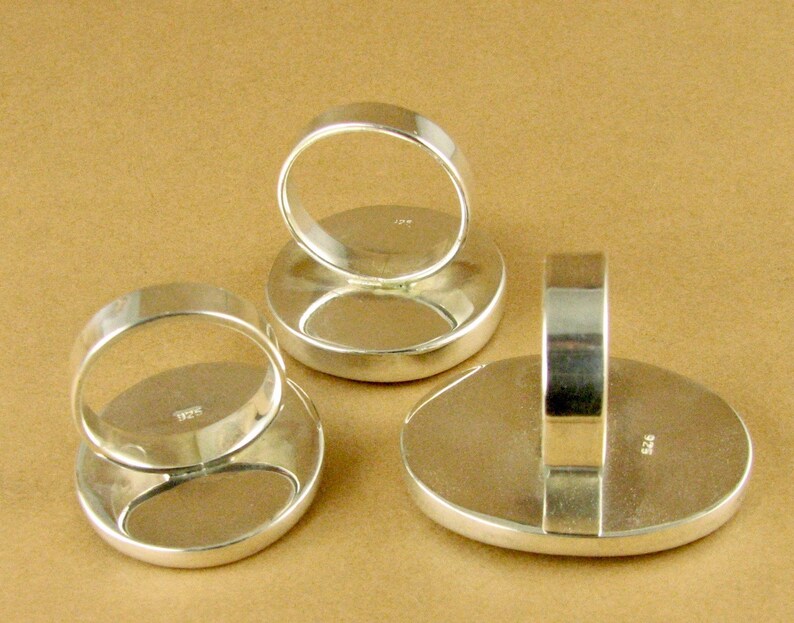 May include: Three silver rings with oval-shaped settings. The rings are shown from the back, revealing the silver bands and the markings "925" on the back of each ring.