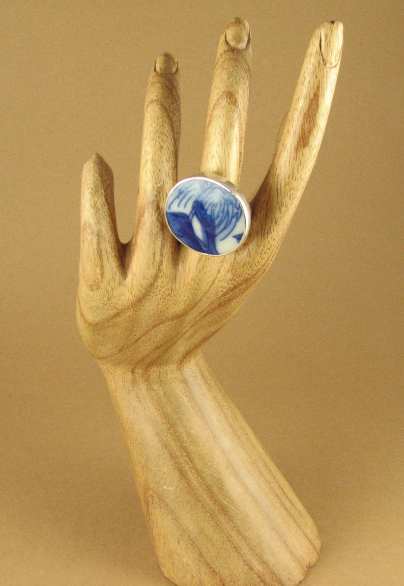 May include: A silver ring with a blue and white ceramic inlay. The inlay features a floral design.