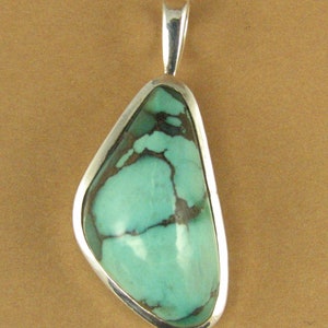 May include: A silver pendant with a turquoise stone. The stone is a light blue-green color with brown veins running through it. The pendant is shaped like a teardrop.