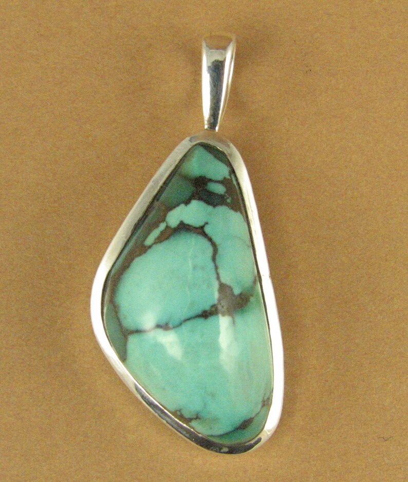 May include: A silver pendant with a turquoise stone. The stone is a light blue-green color with brown veins running through it. The pendant is shaped like a teardrop.