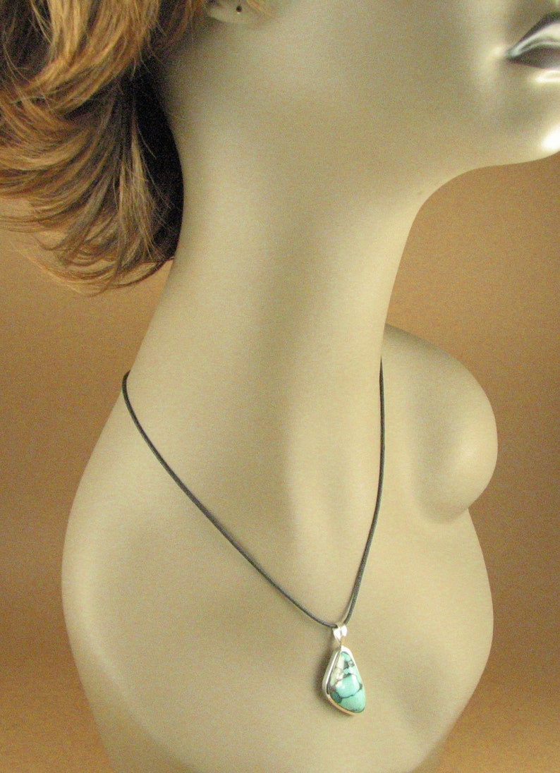 May include: A turquoise gemstone pendant necklace with a silver setting, hanging from a black cord.