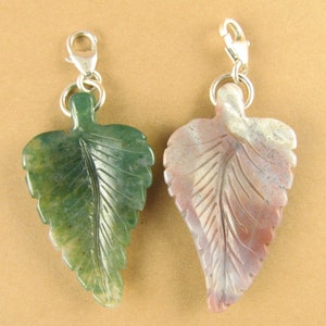 May include: Two carved leaf charms made of agate. The charm on the left is green with brown spots. The charm on the right is pink and white. Both charms have silver clasps.
