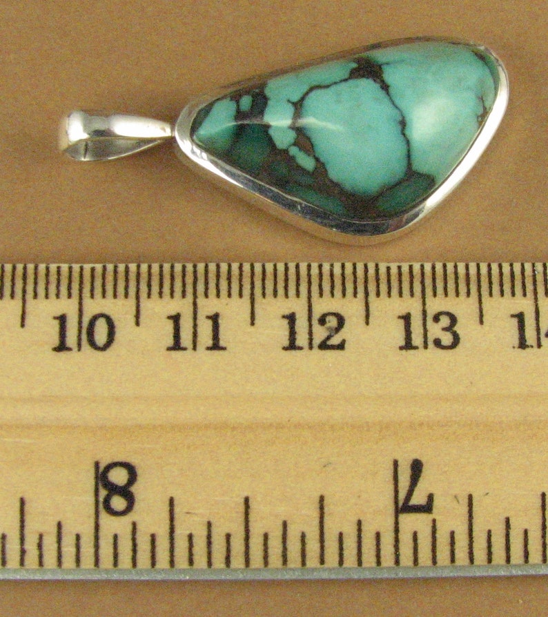 May include: A turquoise pendant with a silver setting. The turquoise is a light blue-green color with brown veins. The pendant is about 1 1/2 inches long.