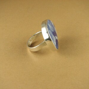 May include: A silver ring with a blue and white ceramic inlay. The inlay is a stylized design of a bird.