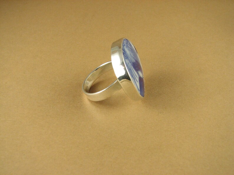 May include: A silver ring with a blue and white ceramic inlay. The inlay is a stylized design of a bird.