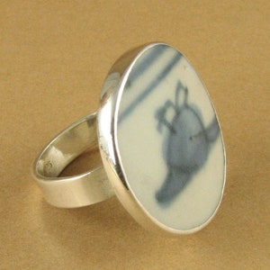 May include: A silver ring with a white ceramic oval inlay featuring a blue and white floral design.
